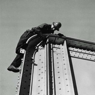 A man in hard hat climbs on a steel girder, surrounded by nothing but sky